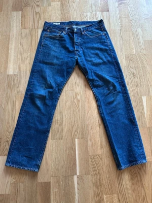 Blå raka 501 jeans från Levi's - Klassiska blå jeans från Levi's med rak passform och gjord av slitstarkt denim. Strl W31 L30.