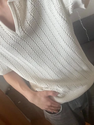 Vit stickad pikéblus med krage - Säljer en vit stickad blus med kort ärm och klassisk krage. Blusen har ett snyggt strukturerat mönster och v-ringning framtill. Materialet känns mjukt och stretchigt, perfekt för en chill och stilren look. Passar till både jeans och kjol. Tips - passar perfekt med en vit/svart tröja underifrån. 
