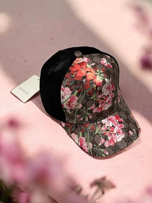 Gucci blommig keps med mesh - Snygg keps från Gucci med klassiskt GG-mönster och färgglada blommor i rosa, rött och vitt. Kepsen har svart mesh på sidorna och justerbar baksida. Perfekt accessoar för att lyfta din stil.