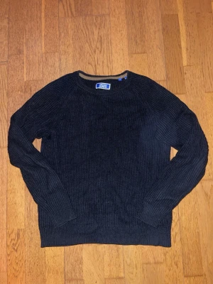 Svart stickad tröja från Jack & Jones - Svart stickad tröja från Jack & Jones med rund halsringning och ribbstickad struktur. Tröjan har långa ärmar och en klassisk, enkel design som passar perfekt till jeans eller chinos. Tröjan passar en person som är ungefär 170 cm och sitter slim så att man visar upp sina muskler.😁