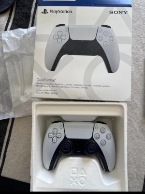 Sony PlayStation 5 DualSense handkontroll - Trådlös DualSense handkontroll till PlayStation 5 i vit och svart design. Ergonomisk form med taktila knappar, inbyggd touchpad och adaptiva triggers. Passar även till PC, Mac och mobil. Perfekt för gaming med avancerad haptisk feedback.