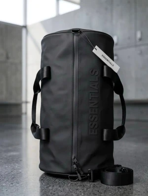 Svart duffelbag från Essentials - Snygg svart duffelbag från Essentials med stilren design och tydlig logga på sidan. Väskan har robusta handtag, avtagbar axelrem och dragkedja från YKK. Tillverkad i ett tåligt, vattenavvisande material som passar perfekt för resor eller gymmet.