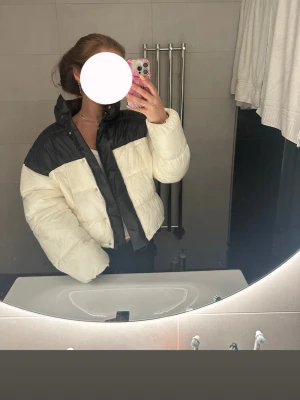 Svartvit pufferjacka med hög krage - Säljer en snygg pufferjacka i svart och vitt med hög krage och dragkedja framtill. Jackan har en boxig passform och breda kanaler som ger en cool look. Perfekt för kalla dagar när du vill hålla dig varm och samtidigt se trendig ut.