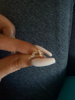 Guldörhängen med tre stenar - Snygga små örhängen i guld med tre gnistrande stenar på varje. Stilren design som ger en elegant touch till din look. Perfekta för dig som gillar diskreta men ändå glittriga accessoarer.