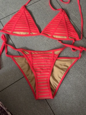 Rosa bikini med ränder från SHEIN - Trendig bikini från SHEIN i stark rosa färg med beige insida. Både överdel och underdel har smala ränder och knytband i sidorna och nacken. Perfekt för stranden eller poolen, med en modern och ungdomlig look.