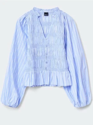 Blå- och vitrandig blus med volang - Supersöt figurnära blå- och vitrandig blus från Gina med smockad front, volangkant nertill och v-ringning. Prislappen är borttagen men har använts vid ett tillfälle,  inga defekter så i princip nyskick. Nypris 400
