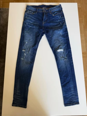 Blå slitna jeans från SMOG - Säljer dessa riktigt schyssta jeansen från SMOG, dom har riktigt feta slitningar och passé perfekt för en chill stil, säljer pga dom är för små, bara att höra av dig vid funderingar!