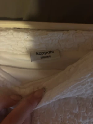 Vit offshoulder topp från Kappahl - Superfin vit offshoulder topp från Kappahl i smockat tyg. Toppen är ärmlös och har en snygg struktur som ger en cool look. Perfekt att styla med jeans eller kjol för en trendig outfit.