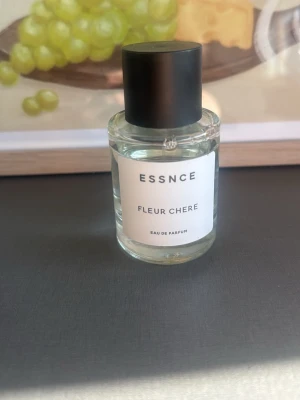 ESSNCE Fleur Chere Eau de Parfum - Minimalistisk parfymflaska från ESSNCE med doften Fleur Chere. Flaskan är genomskinlig med svart lock och vit etikett med svart text. Perfekt för dig som gillar stilrena och enkla designer. Innehåller Eau de Parfum.