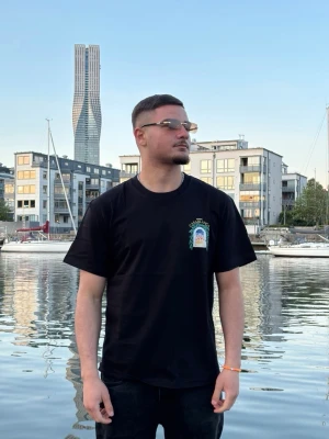 Svart Casablanca t-shirt med tryck - Säljer en svart t-shirt från Casablanca med färgglatt tryck på bröstet och stort motiv på ryggen. T-shirten har klassisk passform och korta ärmar. Perfekt för dig som vill sticka ut med en snygg streetwear-look.