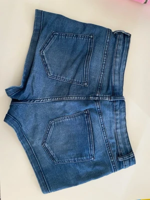 Blå denimshorts - Snygga blå denimshorts och klassiska fickor både fram och bak. Shortsen har bälteshällor.