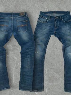Jeans från Nudie  - Snygga blå jeans från Nudie Jeans med klassisk femficksdesign och orangea sömmar. Jeansen har en något tvättad look med slitningar på benen och bakfickor med Nudie Jeans signatursöm. Tillverkade i denim av bomull.
