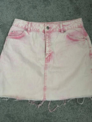 Ljusrosa jeanskjol  - Säljer en ljusrosa jeanskjol med coola slitna kanter och rosa tvättade detaljer. Kjolen har fyra fickor och knappstängning framtill. Perfekt för dig som gillar en avslappnad och trendig stil.