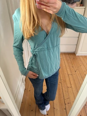 Turkos omlottopp med knyt - Snygg turkos omlottopp med lång ärm och knyt i sidan. Storlek M från simple wishes