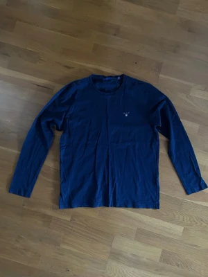 Marinblå långärmad topp från Gant - En stilren marinblå långärmad tröja från Gant med rund halsringning och diskret logga på bröstet. Perfekt basplagg som funkar till det mesta. Tillverkad i mjuk bomull för skön känsla hela dagen.
