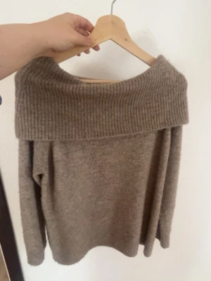 Beige off shoulder stickad tröja - Mysig beige stickad tröja med bred ribbad off shoulder-krage. Tröjan har lång ärm. Perfekt för dig som gillar en avslappnad men ändå trendig stil. Ny utan prislapp!