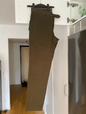 Bruna chinos med rak passform - Snygga mörkgröna chinos med rak passform och klassisk design. Byxorna har sidofickor, bälteshällor och stängs med knapp och dragkedja. Tillverkade i ett mjukt och slitstarkt bomullsmaterial som passar perfekt till en avslappnad men stilren look.