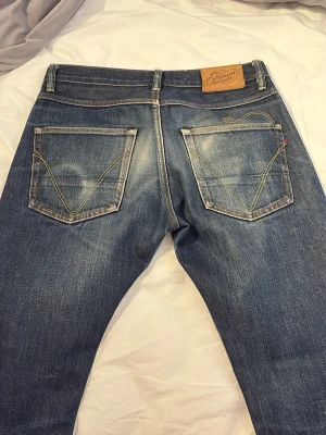  blå denimjeans - Säljer ett par blå selveege denimjeans med regular fit och snygga slitningar. Jeansen har två bakfickor med dekorativa sömmar och klassisk läderpatch i midjan. Perfekta för en avslappnad och trendig stil. Jeansen är i japanskt selvdege tyg storlek 30/32. Jeansen har en snus fade på bakfickan med mer användning kommer dessa bli riktigt feta. Hör av er vid frågor eller funderingar Mått midja 41 längd 101 benöppning 20,5