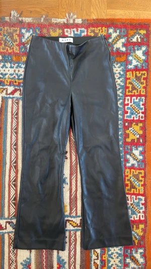 Svarta coated jeans från Wera - Snygga svarta coated jeans från Wera i storlek 34. Byxorna har en bootcut ish passform och glansig finish som ger en cool look. Perfekta för dig som vill ha ett par trendiga byxor med skinnkänsla. Materialet är troligtvis en blandning av bomull och syntet.