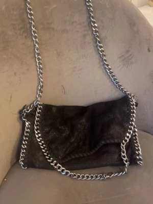 Svart axelväska med kedjedetaljer - Snygg svart axelväska med leopardmönster i. Knappen är sönder som man kan se på bild 3 annars i bra skick