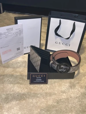 Gucci GG Supreme bälte med svart spänne - Säljer ett Gucci GG Supreme bälte med klassiskt monogrammönster i beige och grå toner. Bältet har ett stort svart GG-spänne och är tillverkat i skinn med canvas-yttermaterial. Perfekt accessoar för att lyfta din outfit med lyxig känsla och ikonisk design.