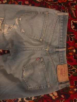 Levi's ljusblå raka jeans vintage - Ljusblå jeans från Levi's med raka ben och klassiska femficksdetaljer. Jeansen har slitningar framtill och en ikonisk läderpatch bak i midjan. Tillverkade i bomullsdenim och har knappgylf. Snygga och vintage.
