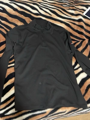 Svart långärmad tröja Parkside - Svart långärmad tröja från Parkside med halv dragkedja framtill och diskret logga på ärmen. Tillverkad i ett stretchigt, tekniskt material som passar perfekt för lager-på-lager och aktiva dagar. Enkel och stilren design.