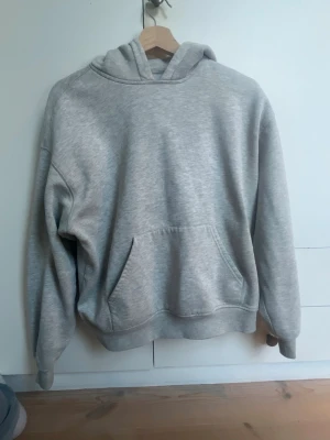 Grå hoodie från gina - En enkel och stilren grå hoodie från Basically Basics. Hoodien har en klassisk huva och en stor magficka framtill. Tillverkad i mjukt material som känns skönt mot huden. Perfekt för en avslappnad och chill look.