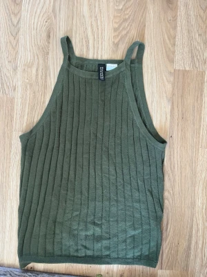 Olivgrön ribbad linnetopp - Snygg olivgrön ribbad linnetopp från Cropped med högt skuren halsringning och smala axelband. Toppen är ärmlös och har en tight passform, perfekt för en trendig och avslappnad look.