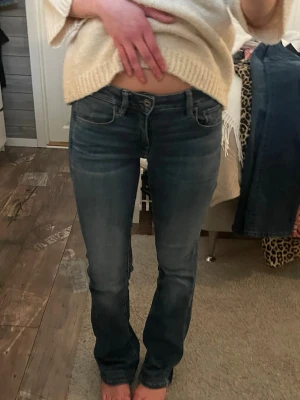 Bootcut jeans med låg midja - Säljer ett par mörkblå jeans med låg midja och raka ben. Jeansen har klassisk femficksmodell och subtila slitningar framtill för en avslappnad look. Perfekta till vardags och passar till det mesta. Materialet är mjukt denim som sitter skönt. Från G Star i storlek w25 l32