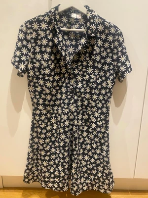 Blommig kortärmad skjorta från hm  - Snygg kortärmad skjorta från hm  med svart botten och vita blommor över hela plagget. Skjortan har klassisk krage och knäppning framtill. Perfekt för dig som gillar färgstarka mönster och vill sticka ut lite extra.