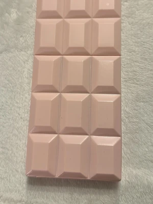 Sweet Tooth parfym av Sabrina Carpenter - Säljer en parfym som heter Sweet Tooth av Sabrina Carpenter. Flaskan är formad som en ljusrosa chokladkaka i plast med geometriska rutor och stilren design. Perfekt för dig som gillar unika och snygga parfymflaskor.