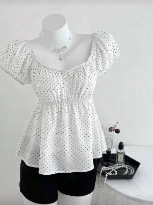 Vit prickig blus med puffärm - Supersöt vit blus med små svarta prickar och puffiga korta ärmar. Blusen har knappar framtill, smockad midja och en lätt utställd passform. Perfekt för en trendig och feminin look., pris kan diskuteras 