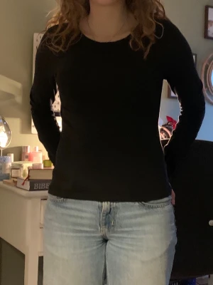 Svart långärmad tröja - En svart långärmad tröja med rund hals och figurnära passform. Tröjan är enkel och stilren, perfekt för dig som gillar en clean look. Materialet ser ut att vara mjukt och stretchigt, vilket gör den bekväm att bära.