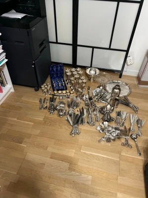 Stort parti bestick och bägare i silver - Säljer ett stort parti bestick, bägare, skålar och serveringsfat i silverfärgat metall. Innehåller gafflar, knivar, skedar, tänger, äggkoppar, vinglas och snapsglas, vissa i blå sammetsask. Perfekt för dig som gillar klassisk dukning och samlar på silverdetaljer.