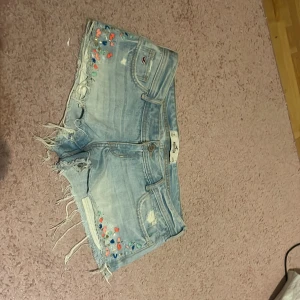 jeansshorts från Hollister - Säljer dessa skit snygga lågmidjade, ljusblåa jeansshorts från Hollister med broderade blommor och pärlor! 