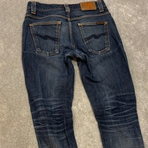 Nudie Grim Tim - Tja! Säljer dessa sjukt snygga mörkblå/blå Nudie ”Grim Tim” jeansen med asfet tvätt! Jeansen är i gott skick, lite slitna vid fötterna (bild 3), men ger dem bara mer karaktär enligt mig. Lagade i skrevet men det märks och syns inte (bild 5). Size 30/32. Skriv vid fler funderingar!