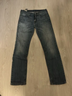 Blå Levi's jeans med raka ben - Snygga blå jeans från Levi's med klassisk femficksdesign och raka ben. Jeansen har en lätt tvättad look med slitningar på låren och diskreta kontrastsömmar. Perfekta för en avslappnad och trendig stil.