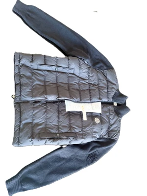 Svart cardigan från Moncler - Kvitto finns me original pris på 8k. Snygg svart cardigan från Moncler med quiltat mönster och stickade svarta ärmar. Cardigan har två framfickor med knappstängning och dragkedja framtill. Klassisk Moncler-logga på bröstet och ribbade muddar vid hals och ärmslut. Perfekt för lager-på-lager-stil.