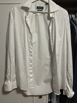 Vit skjorta från Dressmann - Klassisk vit skjorta från Dressmann med lång ärm och knappar framtill. Skjortan har en tidlös design med enkel krage och är tillverkad i ett mjukt bomullstyg. Perfekt för dig som gillar stilrena och enkla plagg.