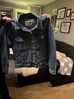 Blå jeansjacka från FB SISTER  - Snygg jeansjacka i klassisk blå denim från FB SISTER. Jackan har silverfärgade knappar, två bröstfickor med lock och knapp samt två sidofickor. Rak passform och bred krage ger en cool och avslappnad look. Perfekt att slänga över en hoodie eller t-shirt.
