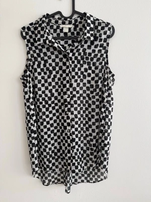 Rutig blus - Lätt och luftig blus från H&M i svartvitt rutigt mönster. Tunt, skönt tyg som faller fint och passar perfekt både till vardag och lite mer uppklätt. Ärmlös modell med krage och knappar framtill.  Skick: Använd men i väldigt fint skick
