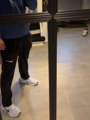 Nike vita och blå sneakers - Fräscha vita sneakers från Nike med blå swoosh och detaljer. Skorna har en klassisk låg siluett och är tillverkade i en kombination av syntet och mesh för bra andningsförmåga. Perfekta för dig som gillar sportig och clean stil.