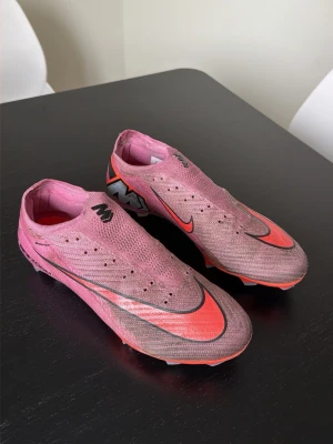 Nike Mercurial rosa fotbollsskor - Säljer ett par Nike Mercurial fotbollsskor i rosa med svarta och röda detaljer. Skorna har en strömlinjeformad design, låg vikt och ovandel i syntetmaterial för bra bollkontroll. Sulan har aggressivt mönster för maximalt grepp på planen. Perfekta för snabba spelare.