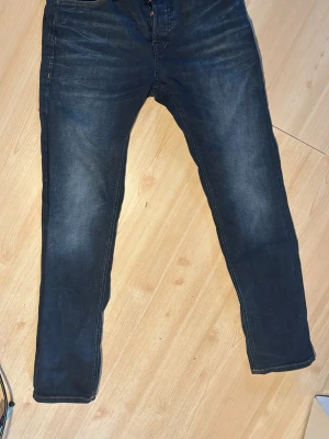 Mörkblå slim fit jeans - Snygga mörkblå slim fit jeans med lätt slitningar och klassiska fem fickor. Jeansen har kontrastsömmar och en modern passform som sitter lite smalare längs benen. Perfekta för en trendig och avslappnad stil.