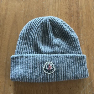 Grå ribbad mössa från Moncler - Grå mössa från Moncler med uppvikta kanter, lätt att matcha till outfit säljes då jag aldrig använder den. Pris kan diskuteras