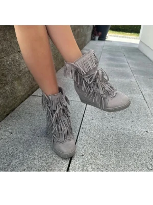 Grå boots med fransar och kilklack - Snygga grå boots med kilklack och massor av fransar längs skaftet och snörningen. Tillverkade i mockaimitation som ger en mjuk känsla och cool look. Perfekta för dig som vill sticka ut med din stil. Knappt använda.