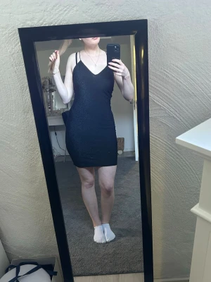 Svart glittrig bodycon klänning - Snygg svart bodycon klänning med tunna axelband och diskret glittereffekt. Klänningen har en figurnära passform och v-ringad halsringning. Perfekt för dig som vill ha en enkel men ändå festlig look. Strl M men passar absolut S.