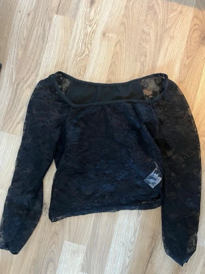 Svart spetsblus med långa ärmar - Trendig svart blus i genombruten spets med långa ärmar och rundad halsringning. Blusen har en lätt transparent look och är perfekt för att skapa en snygg lager-på-lager-stil. Materialet är mjukt och följsamt.