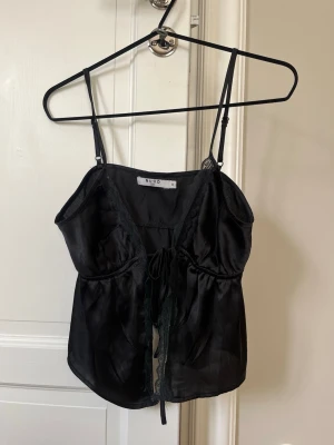 Svart silkesliknande festtopp/ topp - En jättefin svart silkesliknande festtopp med knyte framtill. 💕öppning vid magen och spets utmed kanterna 💕 perfekt skick och helt oanvänd! Storlek 36 (alltså typ S) 